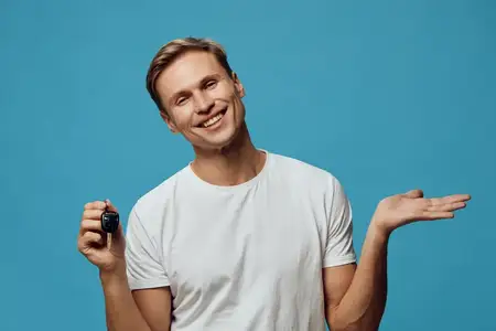 Счастливый улыбающийся мужчина держит в руке ключи от машины, жестикулирует непринужденно и расслабленно с дружелюбным выражением лица на синем студийном фоне