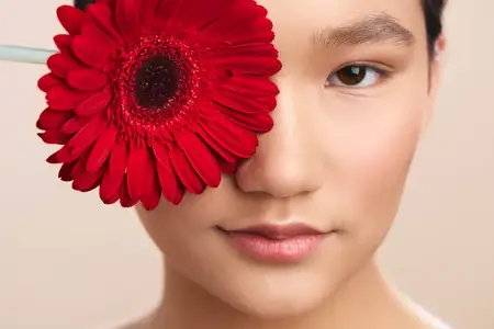 Крупный план с изображением азиатской женщины и яркого красного цветка, передающий грацию, грациозность и изысканный макияж в минималистичном студийном портрете с мягким освещением и детальной…