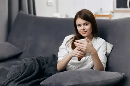 Женщина сидит на диване с мобильным телефоном в руке, чувствуя себя комфортно