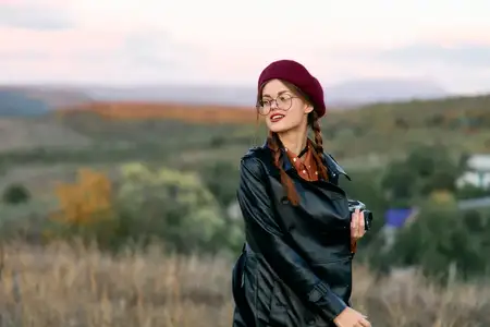 Шикарная женщина в красном берете и кожаной куртке излучает уверенность, стоя на бескрайнем поле