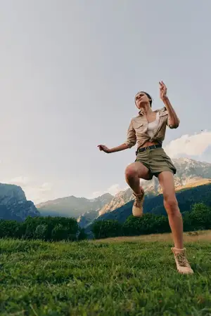 Динамичная outdoor-сцена показывает беззаботную женщину в естественной среде, передавая через движение, солнечный свет и обширный пейзаж идеи здоровья, исследования и молодости