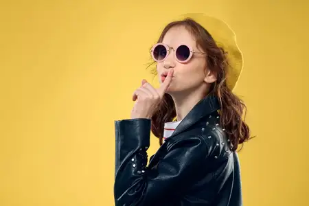 Девочка в желтой шляпе и темных очках, одетая в модную одежду, ведет активный образ жизни в студии