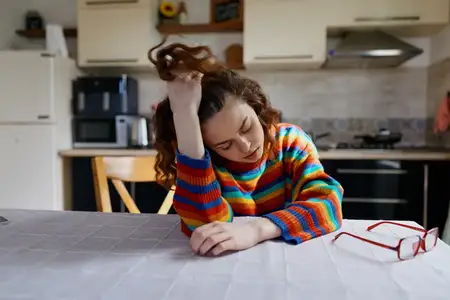 Непринужденная домашняя сцена с задумчивой женщиной за кухонным столом, одетой в полосатый свитер