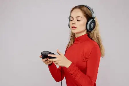 Женщина в наушниках, джойстик в руках, играет в игры, веселье, досуг, образ жизни, развлечения, красная рубашка, серый фон