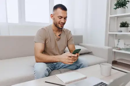 Радостный мужчина взаимодействует со своим смартфоном, удобно устроившись на стильном диване