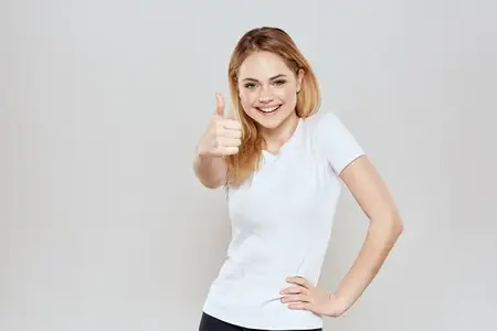 Весёлая блондинка в белой футболке жестикулирует руками на светлом фоне
