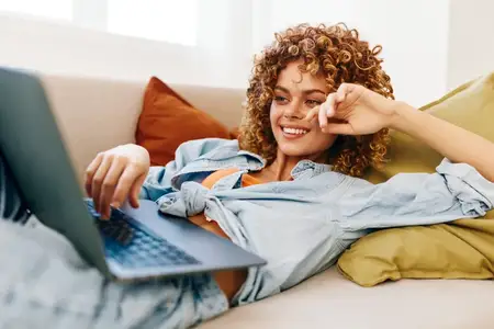 Улыбающаяся женщина работает за ноутбуком в уютном домашнем офисе, оставаясь на связи с онлайн-миром