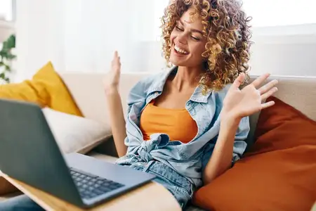 Улыбающаяся женщина работает за ноутбуком в уютной гостиной, наслаждаясь фриланс-работой