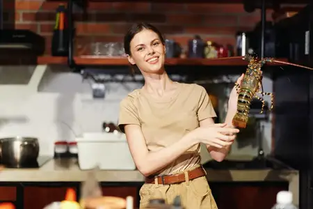 Женщина держит омара на кухне, стоя перед плитой и готовя блюдо из морепродуктов на ужин