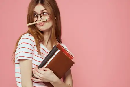 Молодая студентка с книгами на розовом фоне, в очках на лице, кадрированный вид, учебное заведение