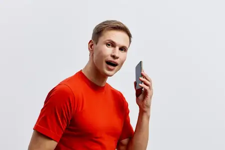 Жизнерадостный мужчина в повседневной красной футболке держит смартфон у лица, улыбается и взаимодействует с камерой
