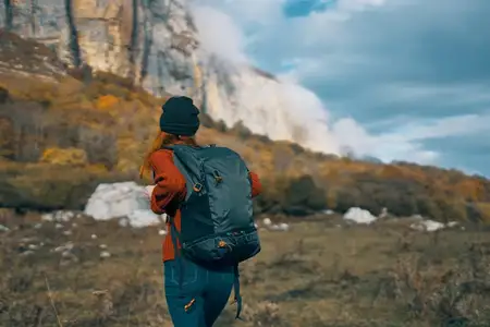 Путешествующая туристка с рюкзаком на фоне высоких гор и неба