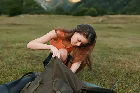 Одинокий путешественник укладывает рюкзак в лугу, проверяя снаряжение и планируя маршрут