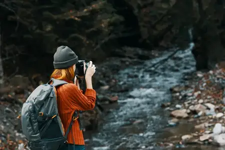 Женщина с фотоаппаратом на природе в горах возле реки и высоких деревьев, лесной пейзаж