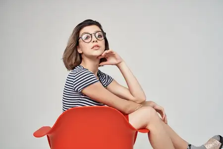 Весёлая женщина сидит на красном стуле, позирует, модный элегантный стиль