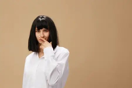 Красивая, сексуальная, стильная, очаровательная брюнетка в белой рубашке позирует изолированно на пастельно-бежевом студийном фоне