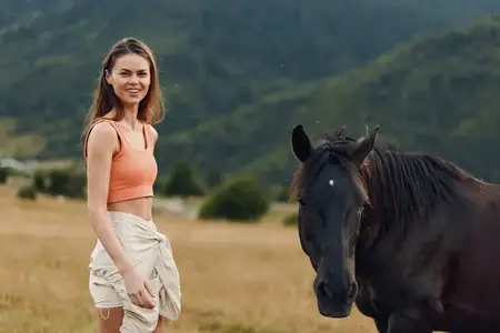 Улыбающаяся женщина любуется лошадью на открытом пастбище на фоне далеких холмов