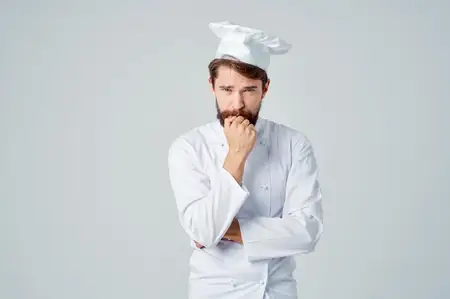 Бородатый мужчина-повар на кухне, жестикулирует руками на светлом фоне