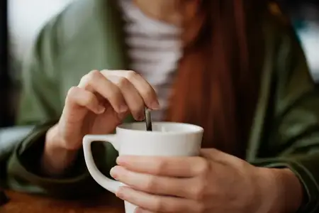 Женщина в кафе размешивает сахар в белой кофейной кружке