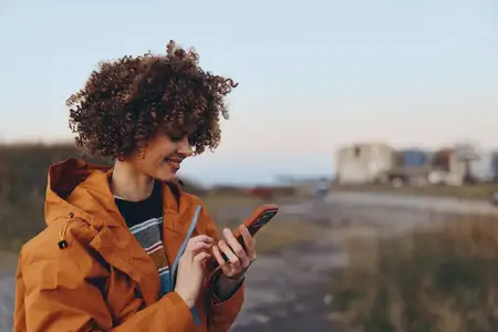 Женщина на открытом воздухе улыбается со смартфоном в руке