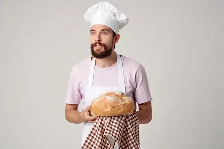 Бородатый мужчина в белом фартуке готовит еду