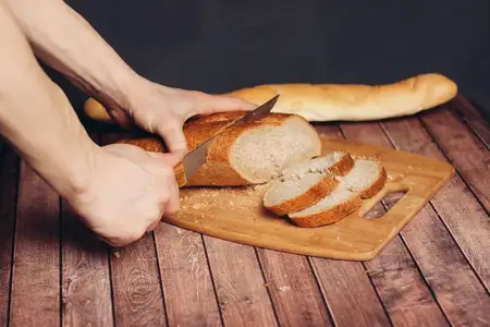 Свежеиспеченный нарезанный батон на деревянном столе, покрытом желтой салфеткой, рядом выпечка