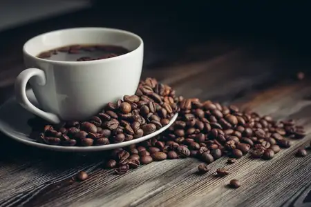 Блюдце с кофейными зернами и белая чашка на деревянном столе, вид сбоку, свободное место
