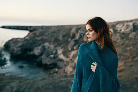 Женщина на закате у моря в горах, с пледом на плечах