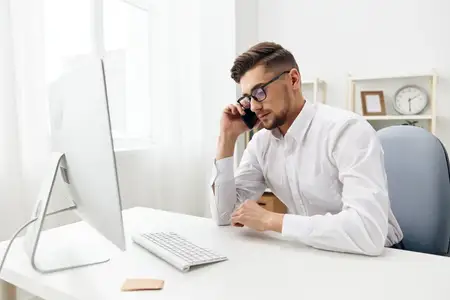 Менеджер в очках сидит за столом в офисе и работает