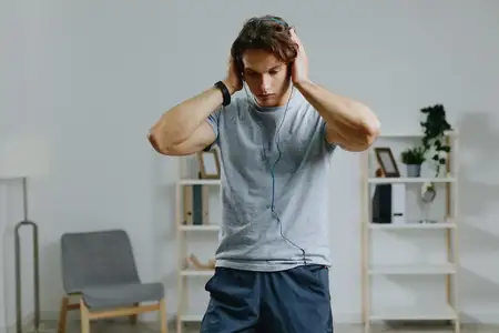 Мужчина в спортивной одежде тренируется дома с гантелями, слушая музыку в наушниках