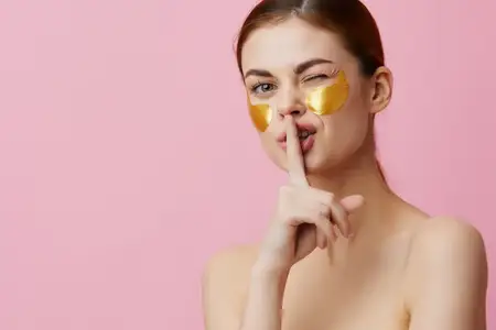 Красивая женщина с патчами для лица, процедура омоложения и ухода за кожей, игривое настроение после душа, на розовом фоне