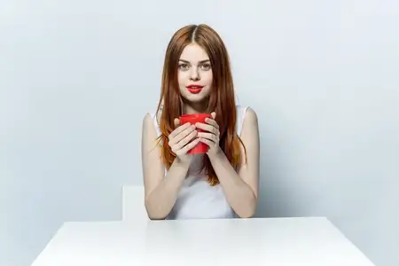Рыжеволосая женщина сидит за столом с чашкой напитка, отдых, эмоции
