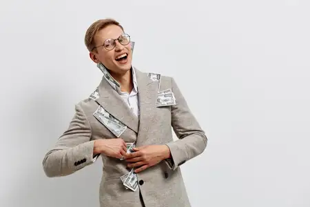 Жизнерадостная женщина с короткими волосами и в очках, одетая в бежевый пиджак, украшенный долларовыми купюрами, демонстрирует счастье и достижение