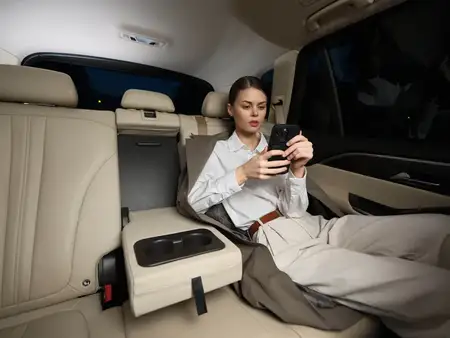 Женщина на заднем сиденье автомобиля держит в руках телефон и смотрит на него