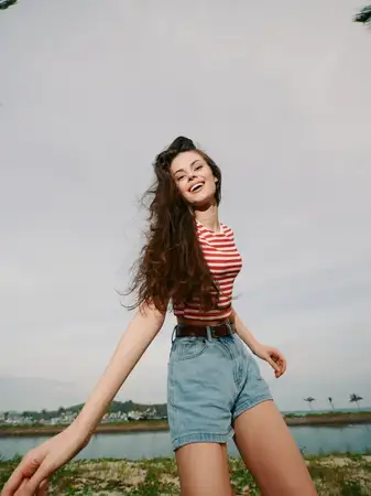 Яркое беззаботное настроение с открытым пейзажем, игривой позой, теплым светом, ветреной летней атмосферой, повседневной модой, солнечным светом, жизнерадостной энергией