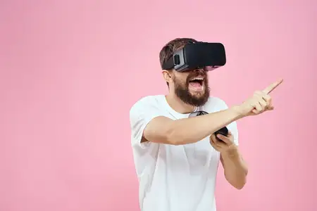Мужчина в очках виртуальной реальности с джойстиком, играет в видео, образ жизни, белая футболка, розовый фон