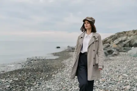 Модная женщина в пальто и шляпе прогуливается вдоль каменистого берега