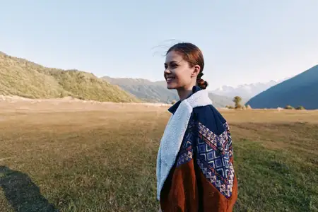 Женщина, улыбка, пейзаж, горы, луг, свитер, на открытом воздухе, портрет — Портрет счастливой женщины в теплом свитере, идущей по открытому лугу недалеко от альпийских гор, наслаждающейся походным…
