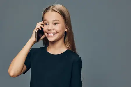 Улыбающаяся девушка держит телефон возле уха на сером фоне