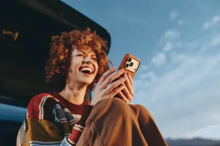 Портрет смеющейся женщины, которая делает селфи на смартфон на открытом воздухе рядом с автомобилем