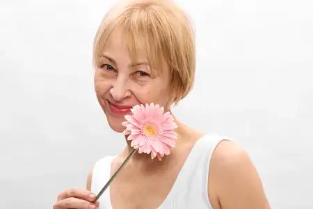Женщина с розовым цветком, улыбка, блондинка, студийный портрет на белом фоне, зрелая, жизнерадостная, крупный план