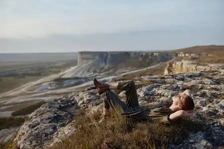 Женщина отдыхает на вершине горы, вытянув ноги и положив руки на колени, наслаждаясь красотой природы