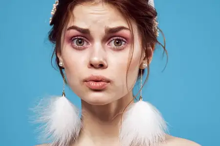 Симпатичная женщина с обнажёнными плечами, пушистыми серьгами и ярким макияжем