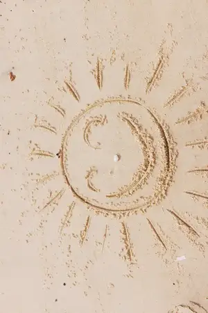 На пляже на песке нарисованы смайлик с улыбкой и слова «happy» и «smile», а на заднем плане светит солнце