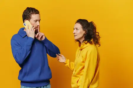 Мужчина и женщина, пара, с телефоном в руке, разговаривают по телефону на жёлтом фоне