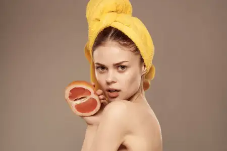Симпатичная женщина с обнаженными плечами, занимающаяся уходом за кожей, держит в руке грейпфрут, кадрированный вид