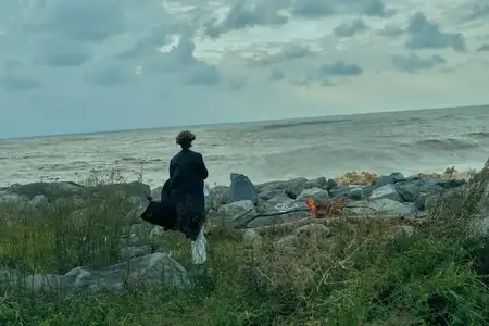 Одинокая фигура на ветреном побережье, скалы и море, развевающаяся куртка, далекий горизонт, созерцательное настроение, исследование природы на открытом воздухе