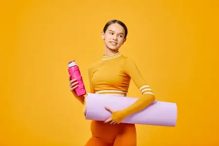 Динамичная фитнес-сцена с улыбающейся женщиной в спортивной одежде, с бутылкой воды и ковриком для йоги, готовой к тренировке и занятиям в яркой оранжевой обстановке