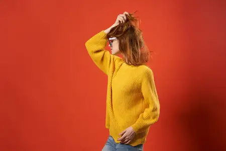 Симпатичная женщина в желтом свитере, модные очки, красный фон