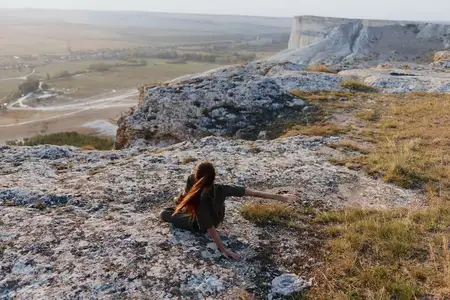 Женщина сидит на краю скалы с раскинутыми руками